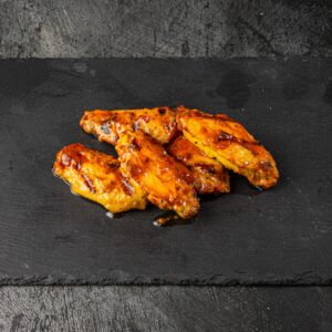 Five glazed peri peri chicken wings on slate board at Bross Slice and Grill